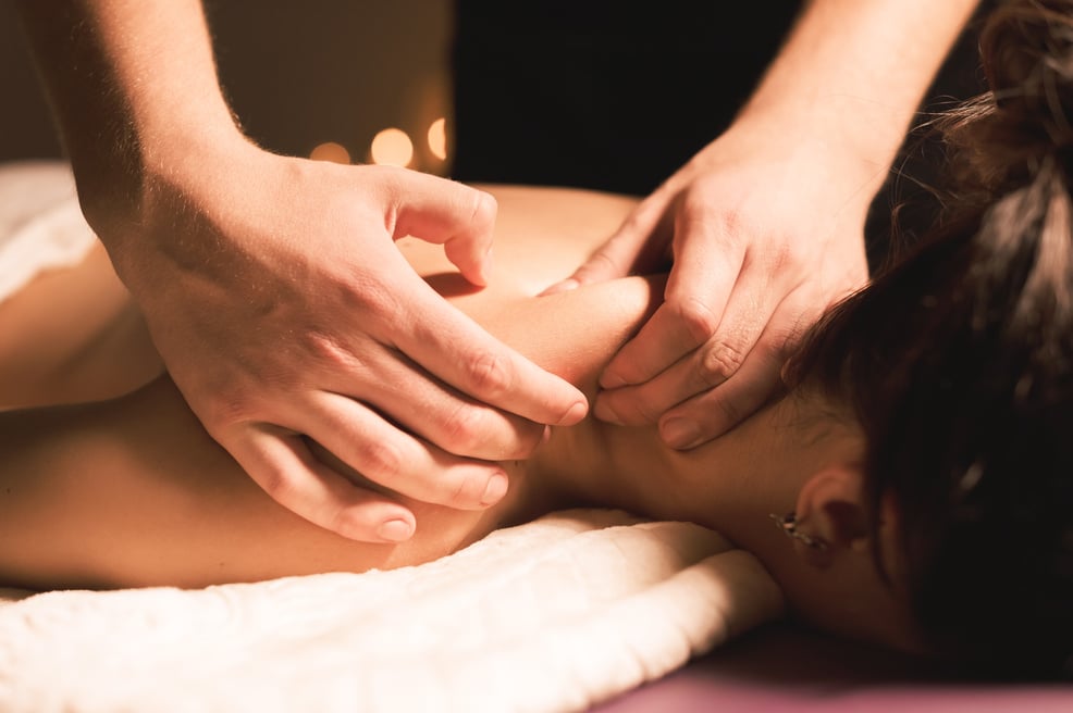 Men's hands make a therapeutic neck massage for a girl lying on a massage couch in a massage spa with dark lighting. Close-up. Dark Key